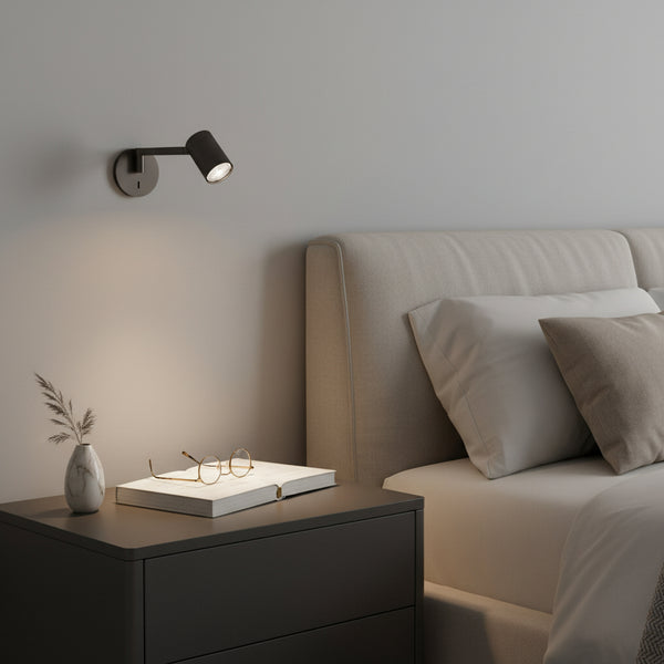 Black wall-mounted reading light above a dark grey nightstand with a book and glasses
