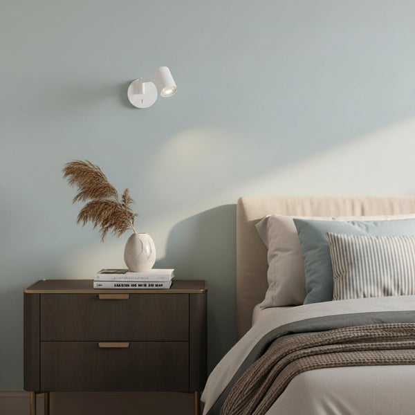 Bedroom with a bed, a nightstand with a vase and books, and a wall-mounted light fixture