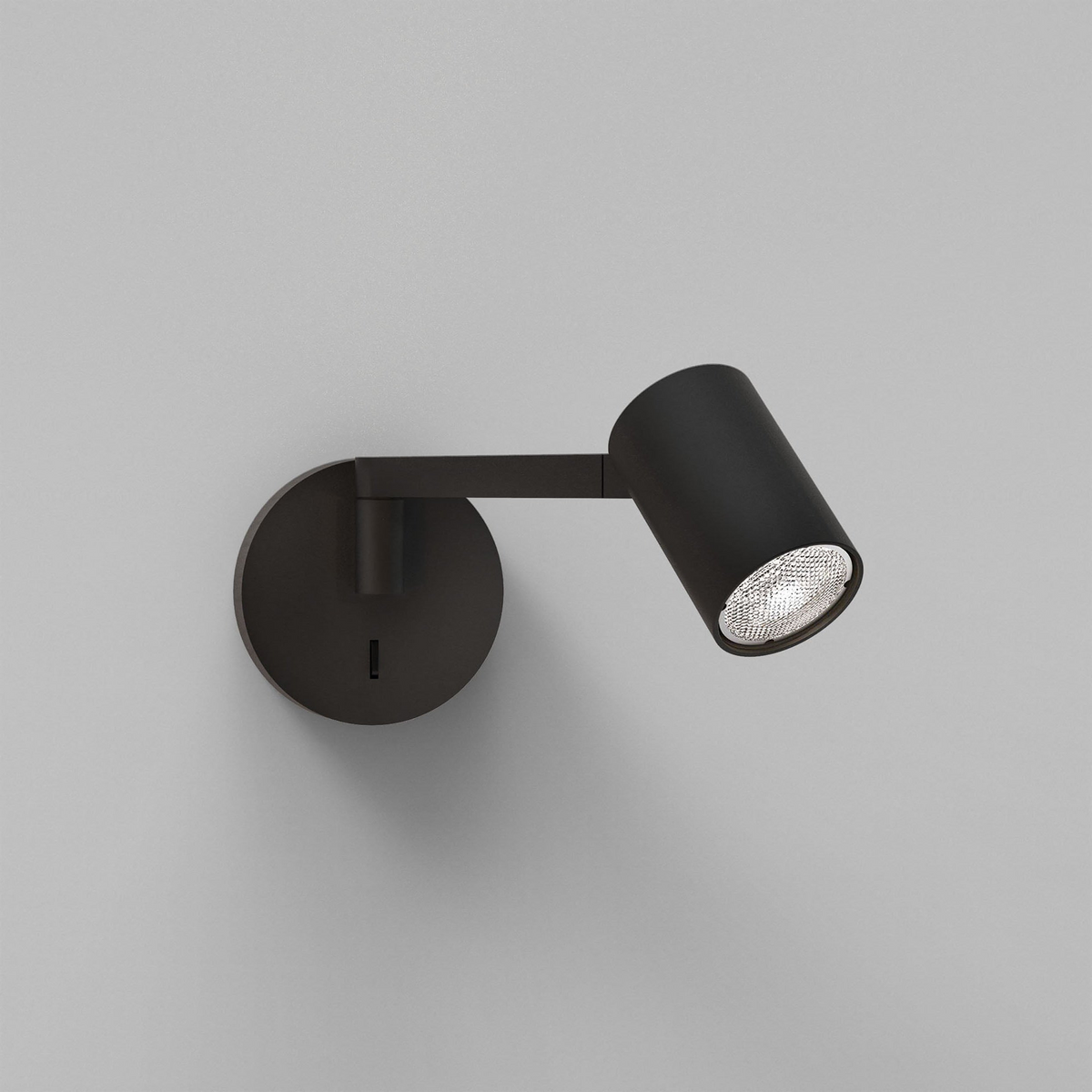 Black wall-mounted spotlight with an adjustable arm and a textured bulb, against a light grey wall