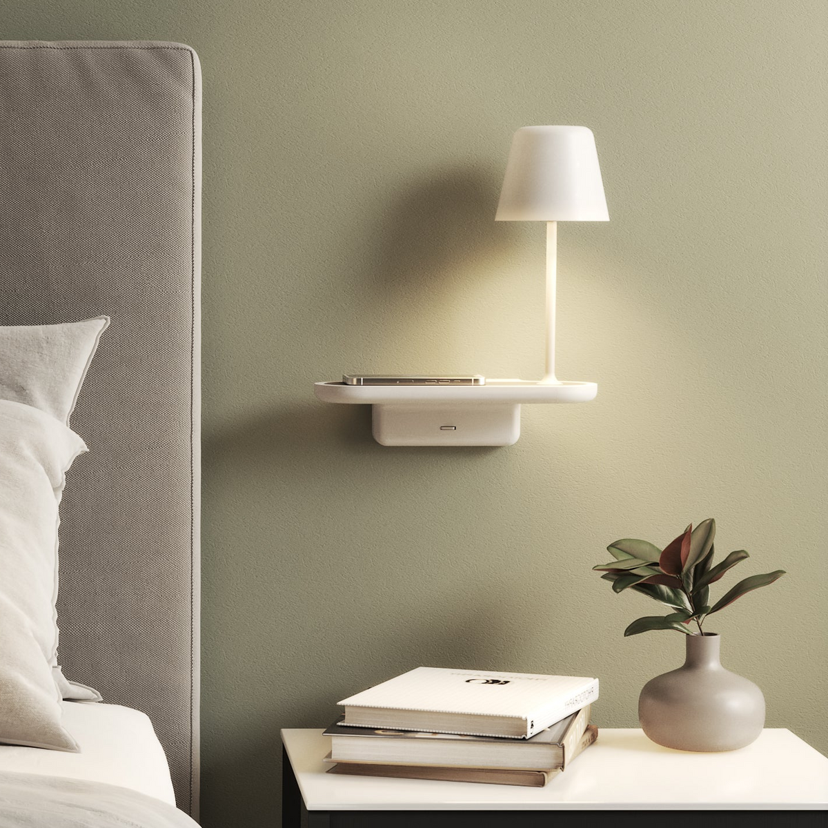 A white wall-mounted shelf with a lamp and phone, next to a bed with a grey headboard and a plant