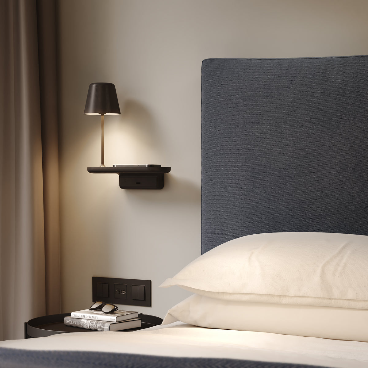 Bedroom with a bed, a wall-mounted lamp, and a side table with books and sunglasses