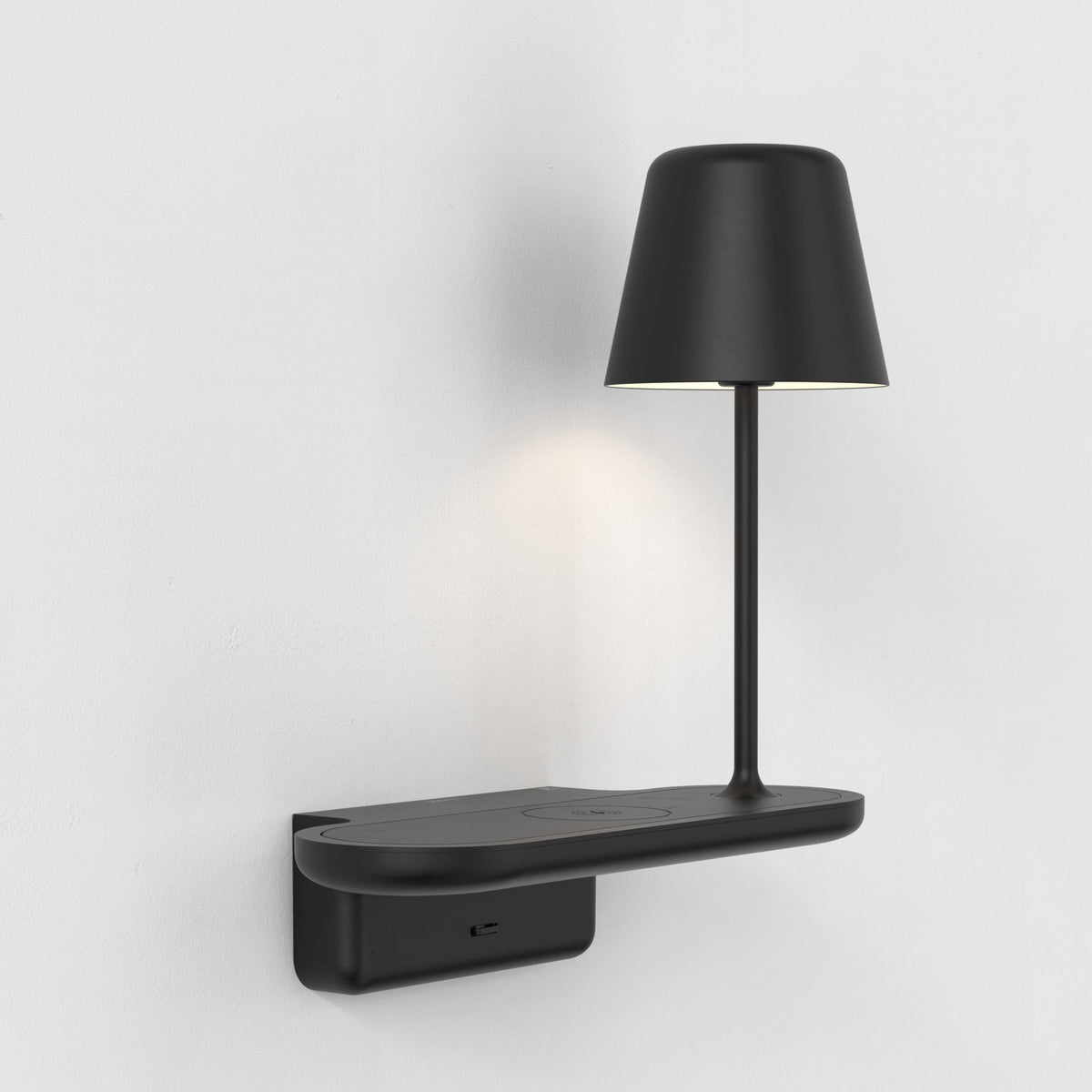 Black wall-mounted lamp with a circular base and a cylindrical shade, emitting a soft glow
