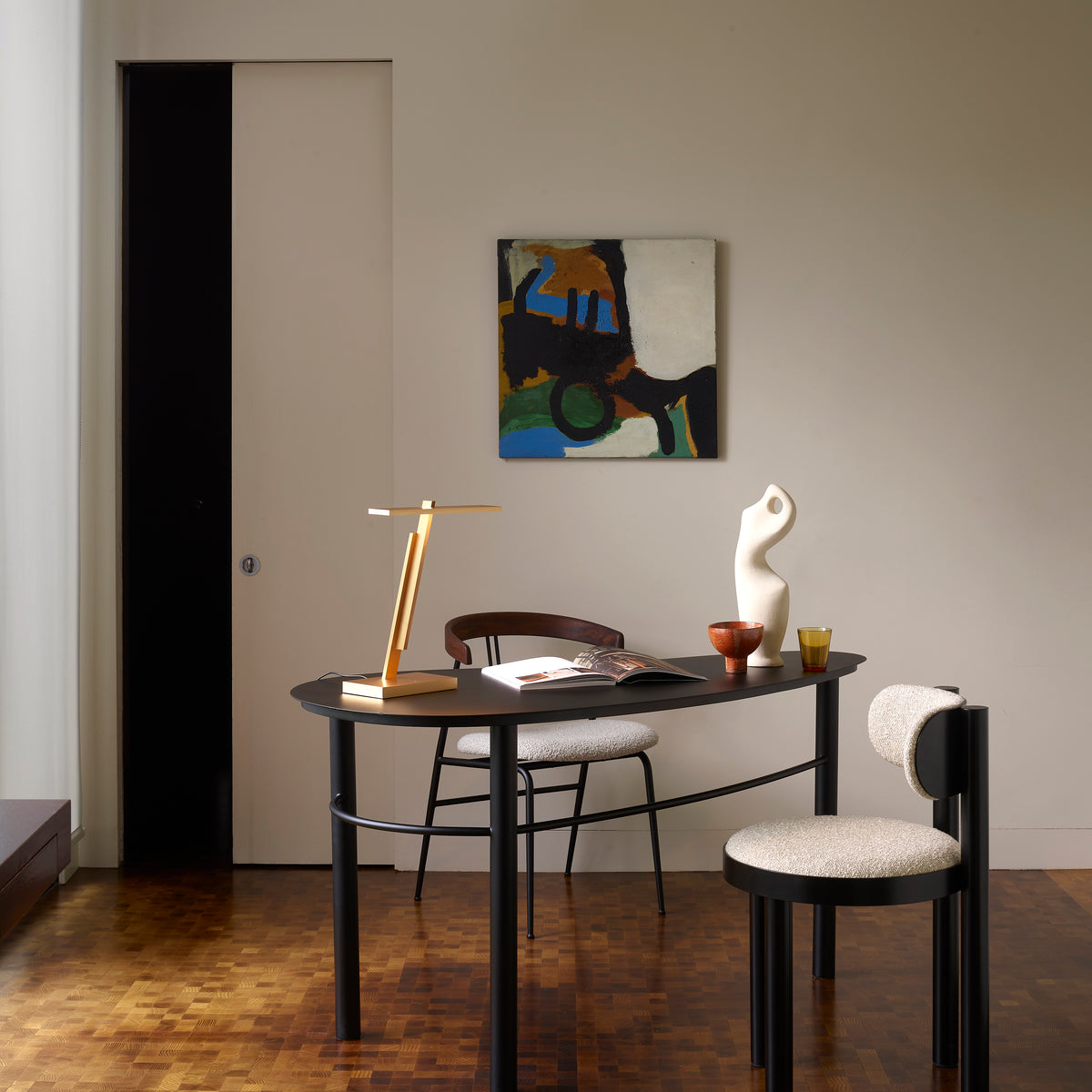 A modern office space with a black desk, two chairs, a lamp, and an abstract painting on the wall