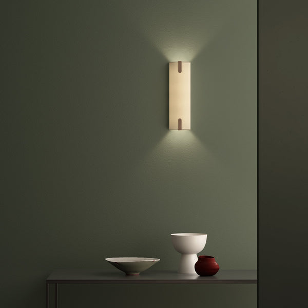 Wall sconce with a warm glow on a dark green wall, above a console table with decorative bowls