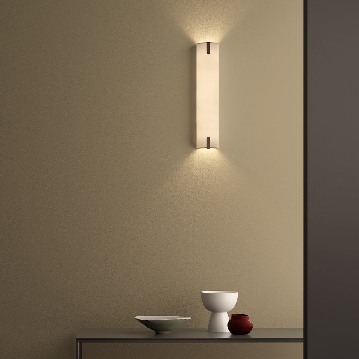 A modern wall sconce illuminates a textured beige wall above a console table with decorative bowls