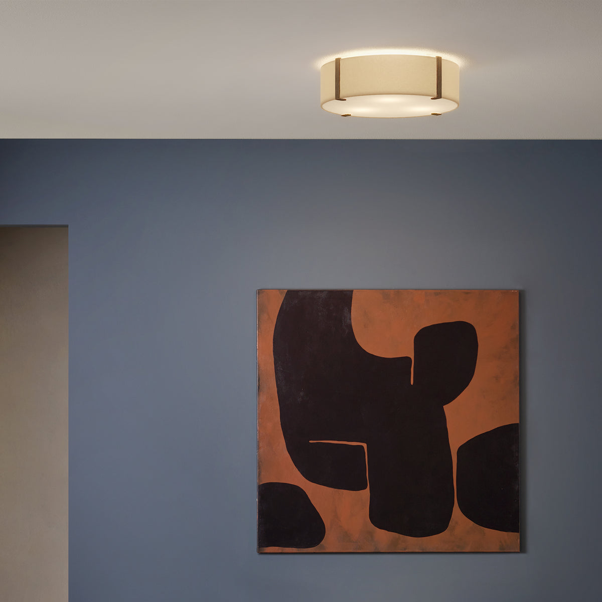 A ceiling light with a fabric shade and wooden accents illuminates a blue wall with abstract art