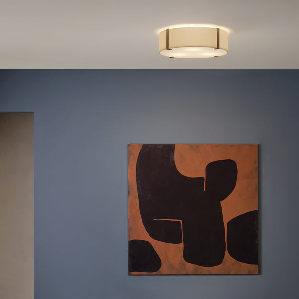 A ceiling light with a fabric shade and wooden accents illuminates a blue wall with abstract art