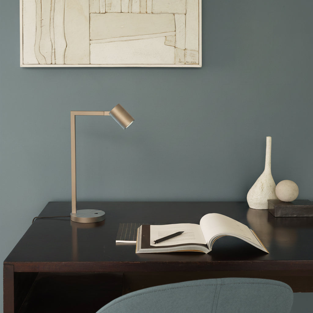 A desk lamp with a cylindrical head and a rectangular arm on a dark wooden desk