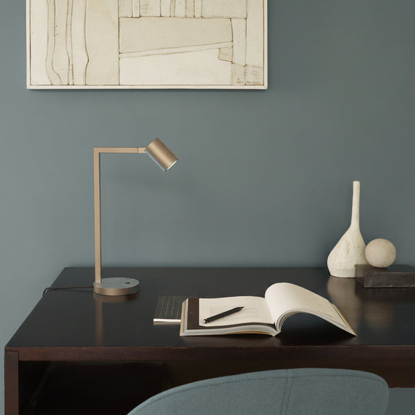 A desk lamp with a cylindrical head and a rectangular arm on a dark wooden desk
