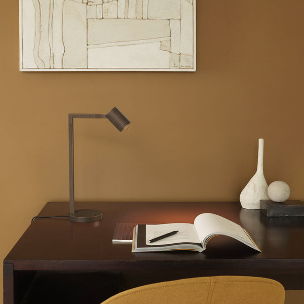Desk lamp illuminating an open book with a pen on a dark wooden desk