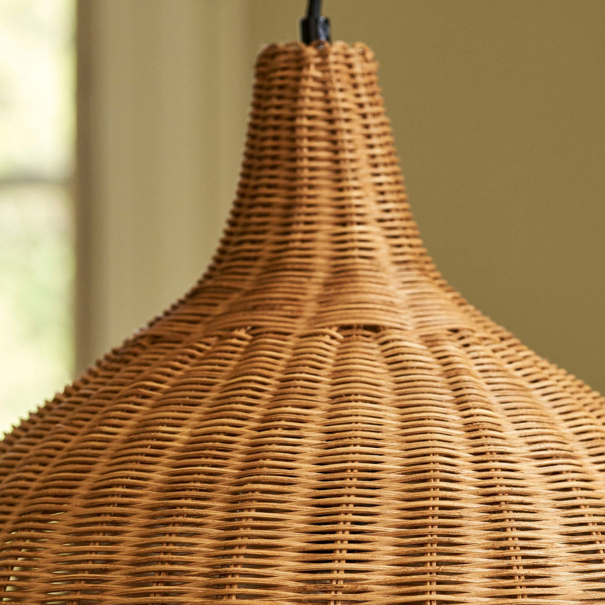 A close-up of a woven wicker pendant lamp shade in a warm natural tan color, hanging against a soft beige background.