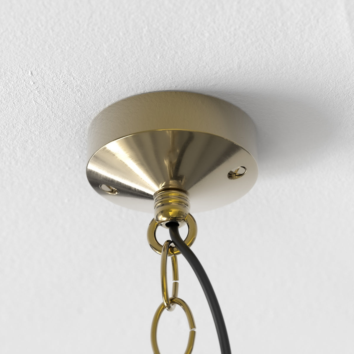 Close up of a gold ceiling rose with a black cable and gold chain hanging from it