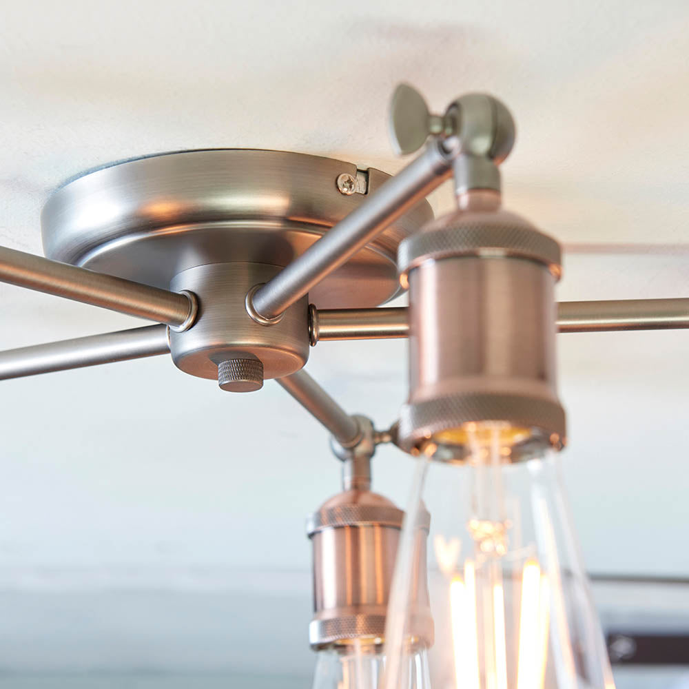 A close-up of the base and one arm of a bronze semi-flush ceiling light with an exposed bulb.