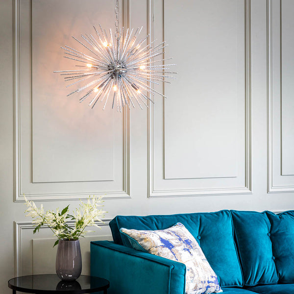 Chrome Sputnik chandelier with clear glass rods illuminates a living room with a teal sofa and white paneled wall.