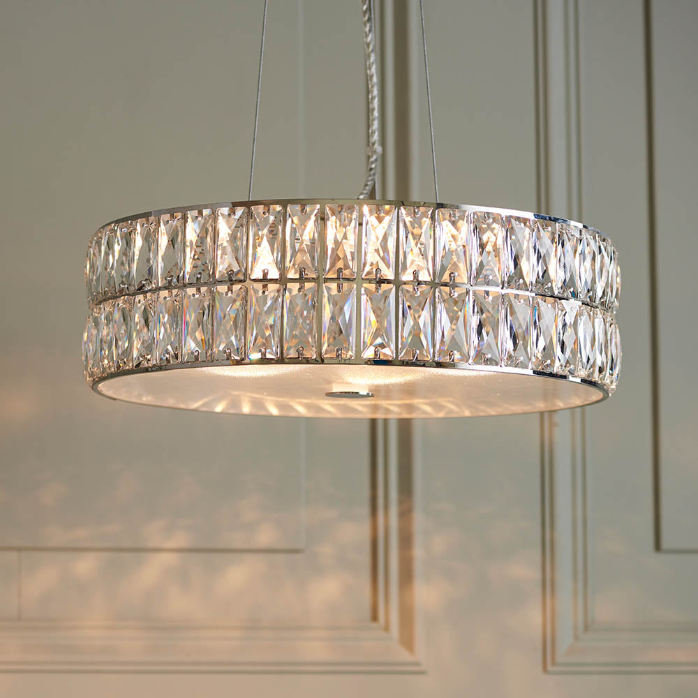 A close-up of a round, two-tiered crystal chandelier with a silver frame, casting light on a paneled wall.