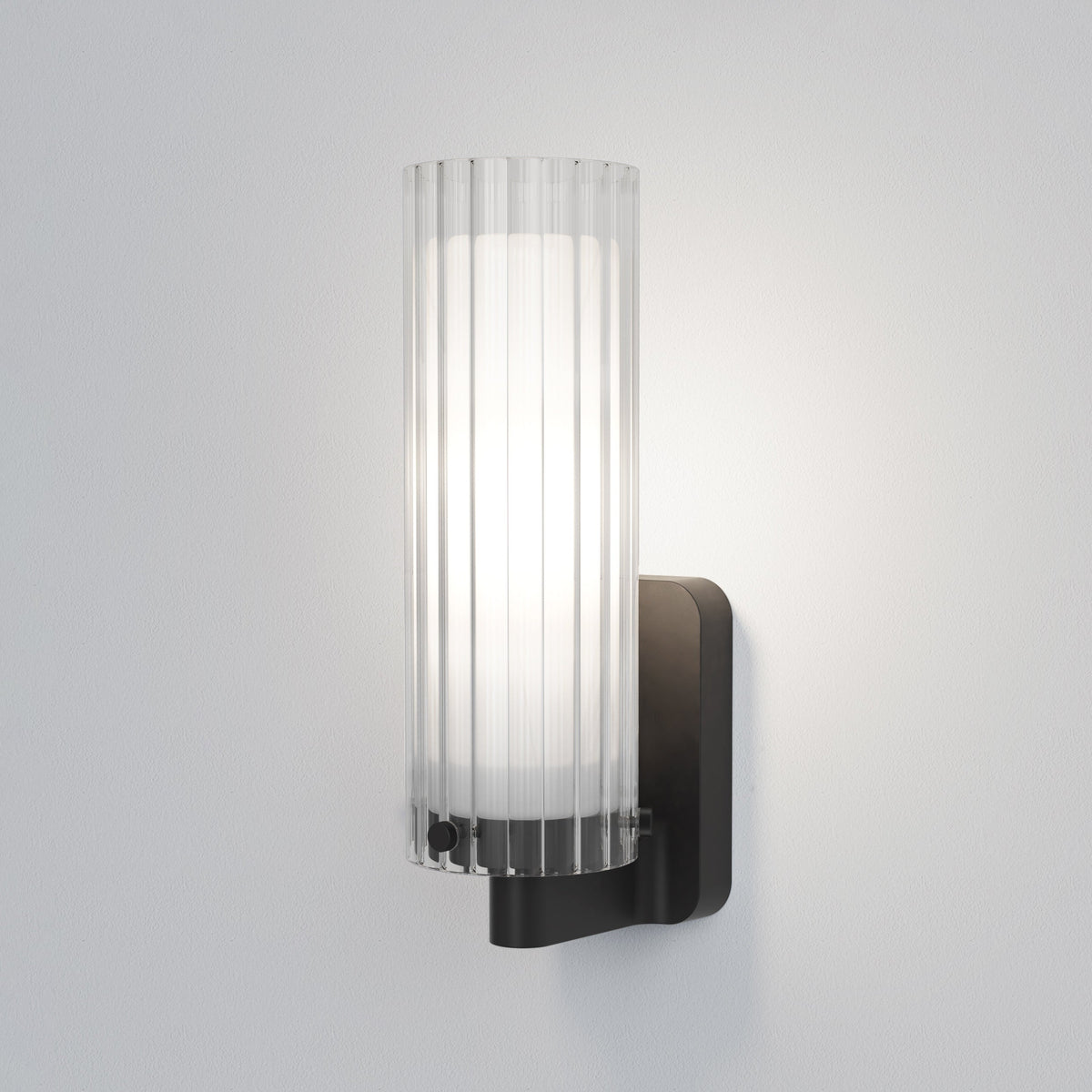 Black wall sconce with a ribbed glass shade and a white light glowing from within