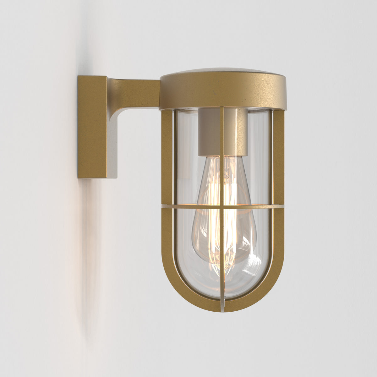 A gold wall light with a clear glass shade and a visible filament bulb