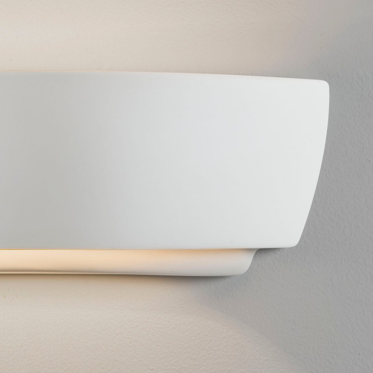 White wall light with a curved top and a straight bottom edge, casting a warm glow downwards onto a textured wall