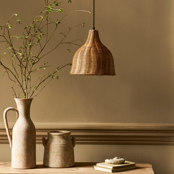 Mouldon Small Pendant in Rattan by Garden Trading Lighting hanging above a wooden table with vases