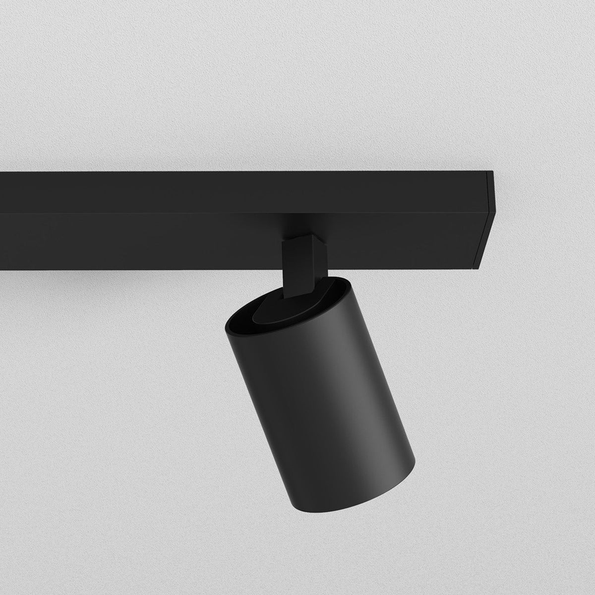 Black cylindrical spotlight attached to a black track light system on a white ceiling