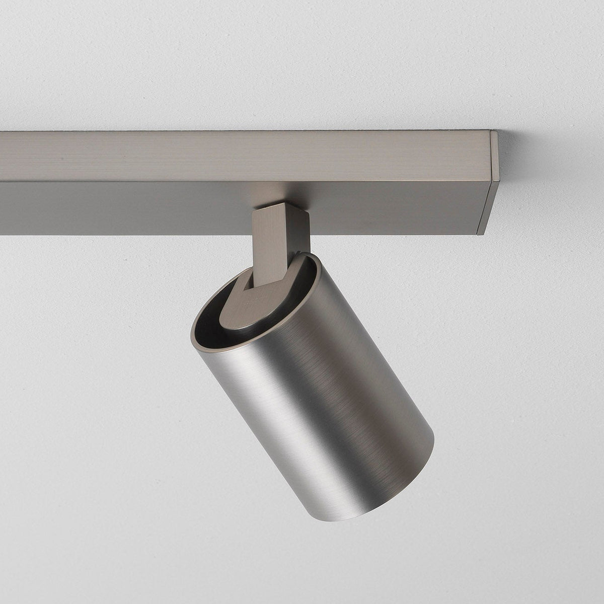 Brushed metal track light fixture with a cylindrical spotlight attached to a rectangular track on a white ceiling