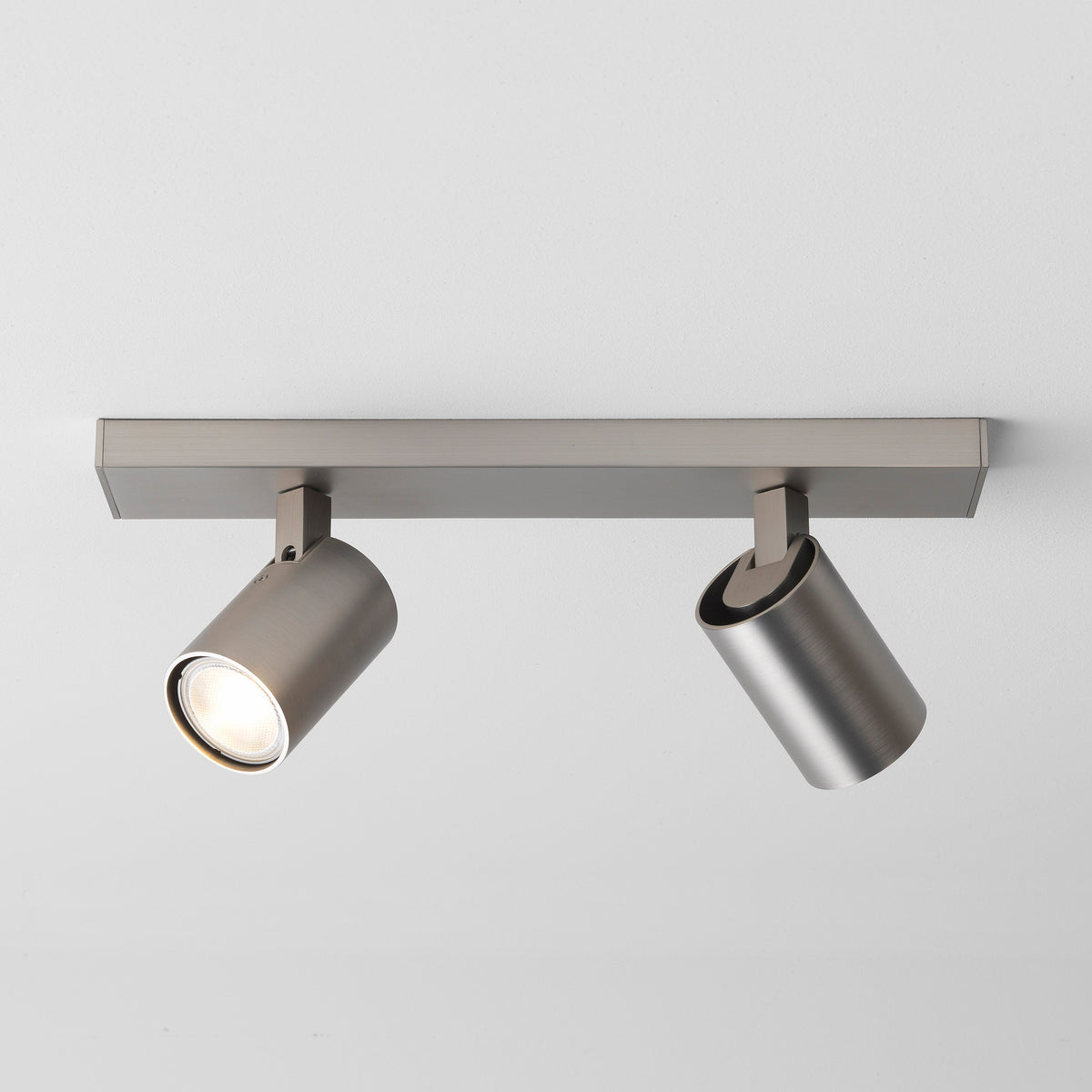 Two brushed metal cylindrical spotlights on a rectangular bar, one illuminated, mounted on a white ceiling