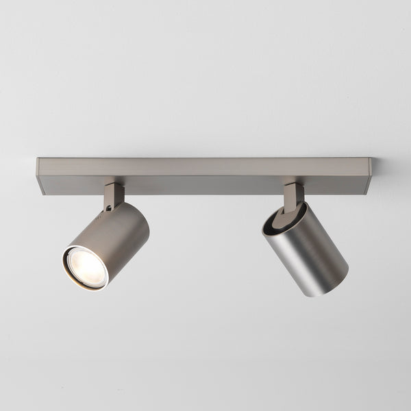 Two brushed metal cylindrical spotlights on a rectangular bar, one illuminated, mounted on a white ceiling