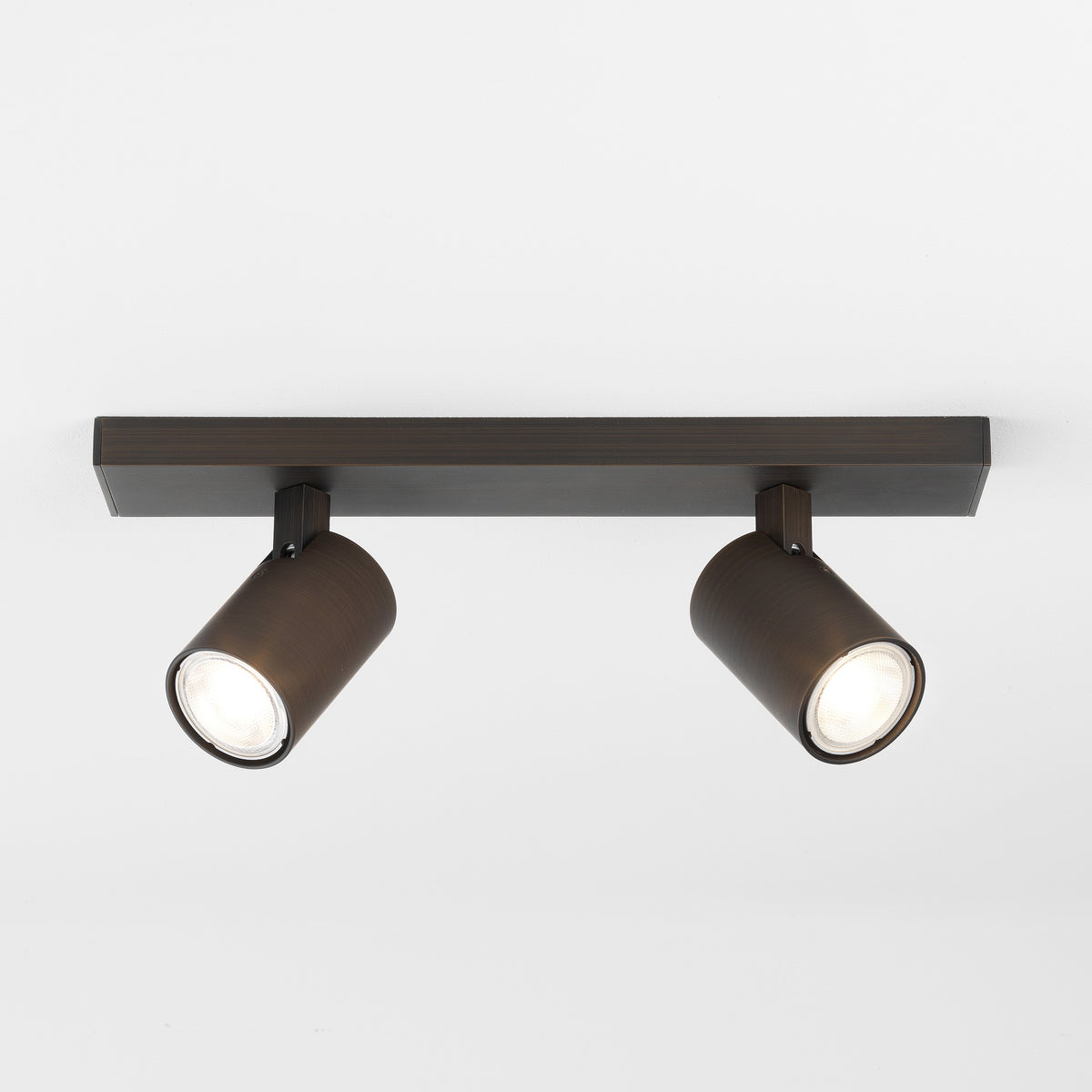 Two dark bronze cylindrical ceiling spotlights with bright bulbs on a white ceiling