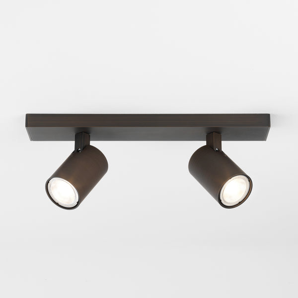 Two bronze cylindrical ceiling spotlights with bright bulbs on a white ceiling