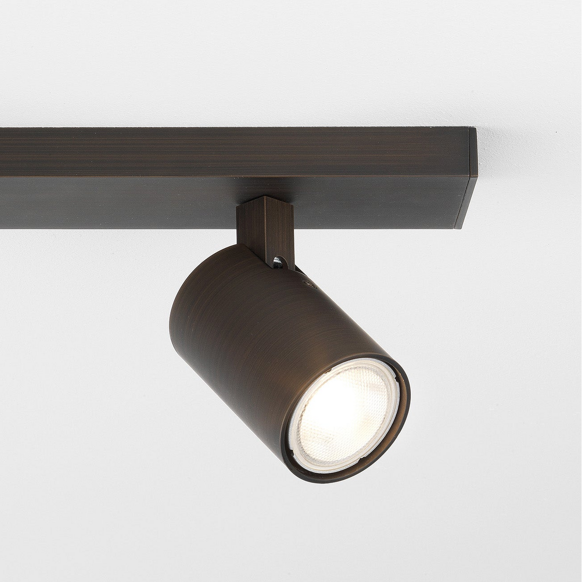 Bronze track light with a cylindrical head and a bright bulb