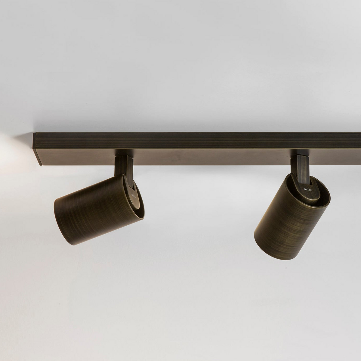 Two bronze cylindrical spotlights attached to a bronze track light fixture on a white ceiling