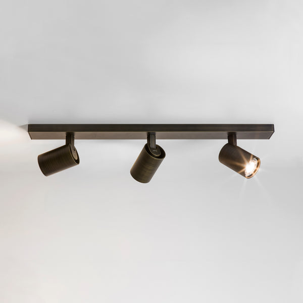 Three bronze track lights on a white ceiling, one light is on