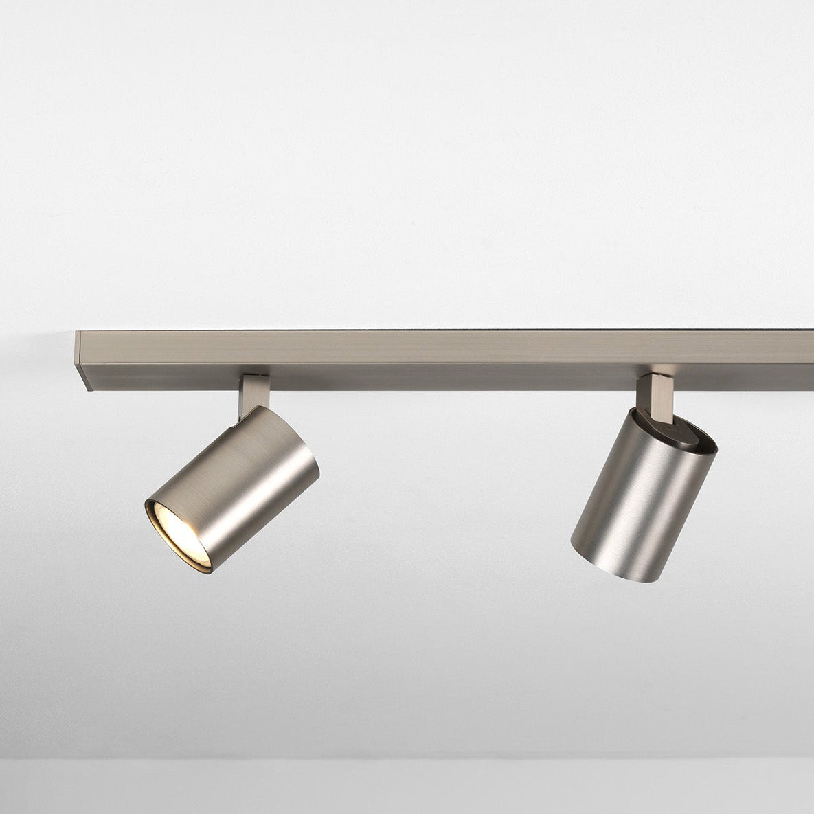 Two brushed metal track lights on a white ceiling, one illuminated