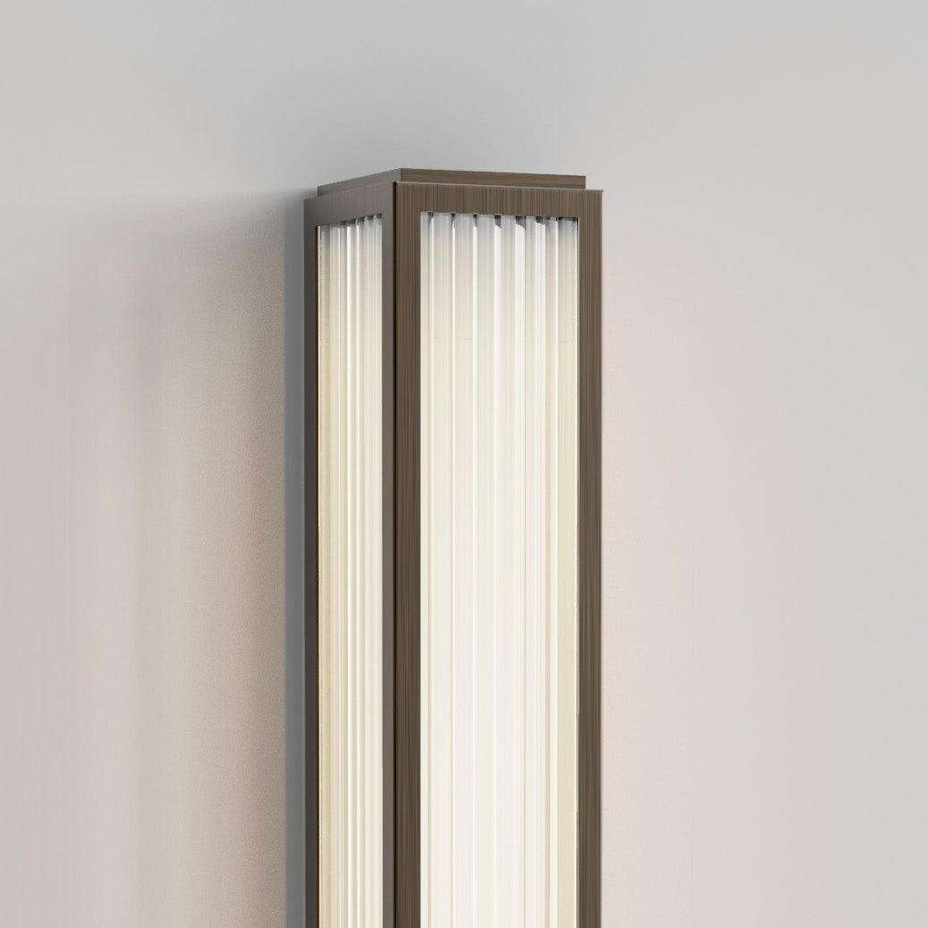 Rectangular wall sconce with a bronze frame and vertical ribbed glass panels, emitting a soft glow