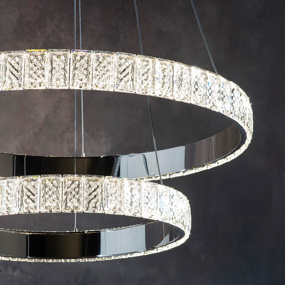 Close-up of two illuminated crystal ring chandeliers against a dark, textured wall.