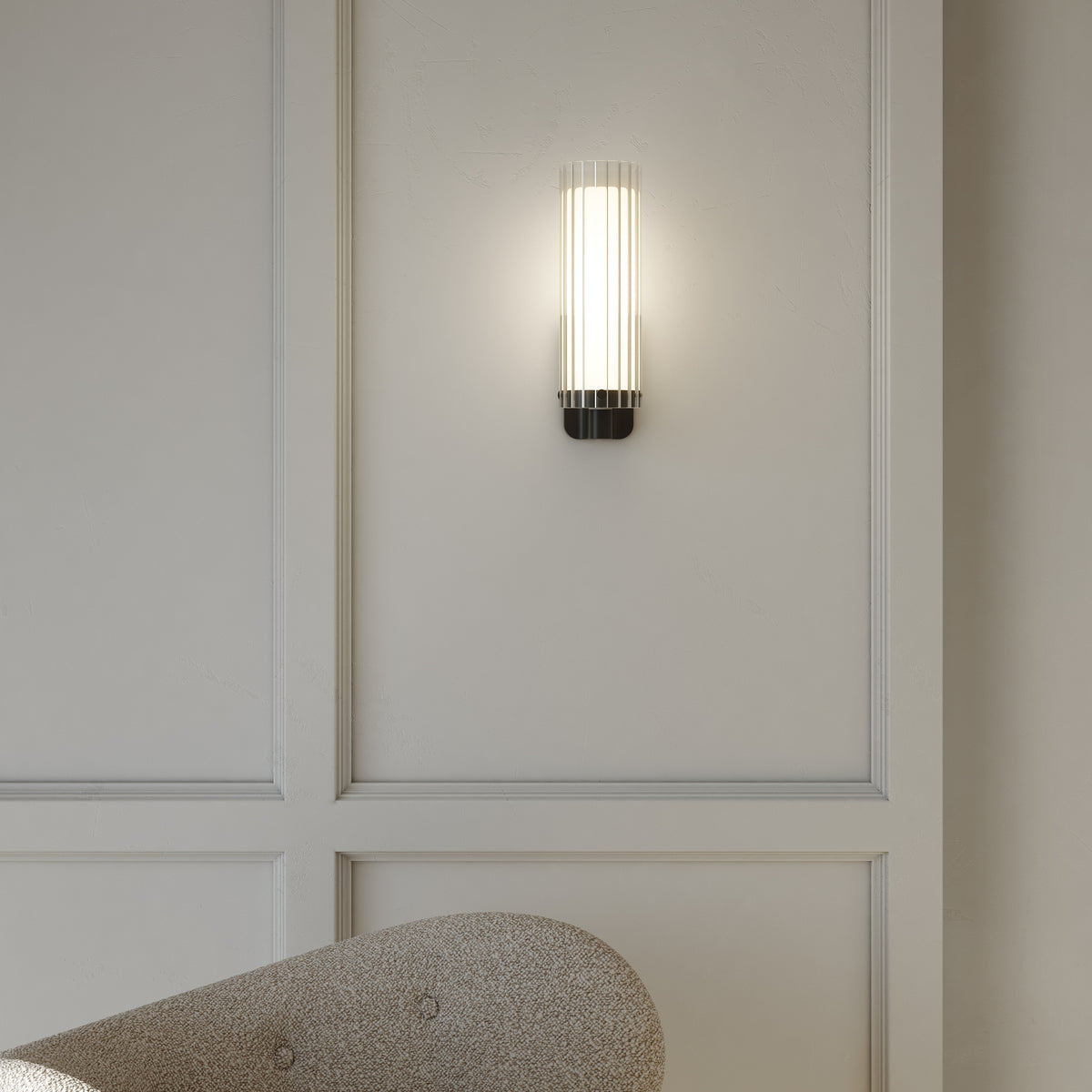 A modern wall sconce with a ribbed glass shade and a black base illuminates a textured wall