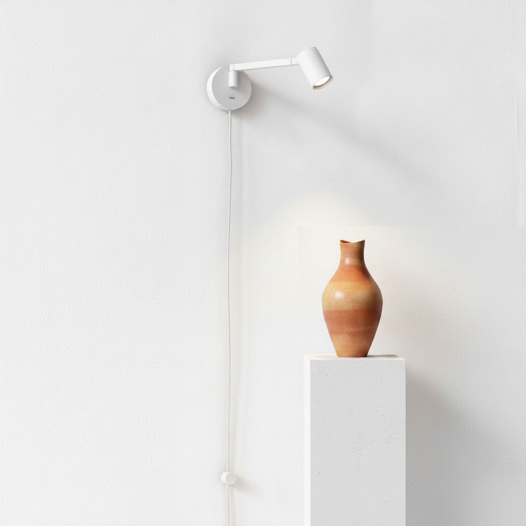 White wall-mounted spotlight illuminating a terracotta vase on a white pedestal