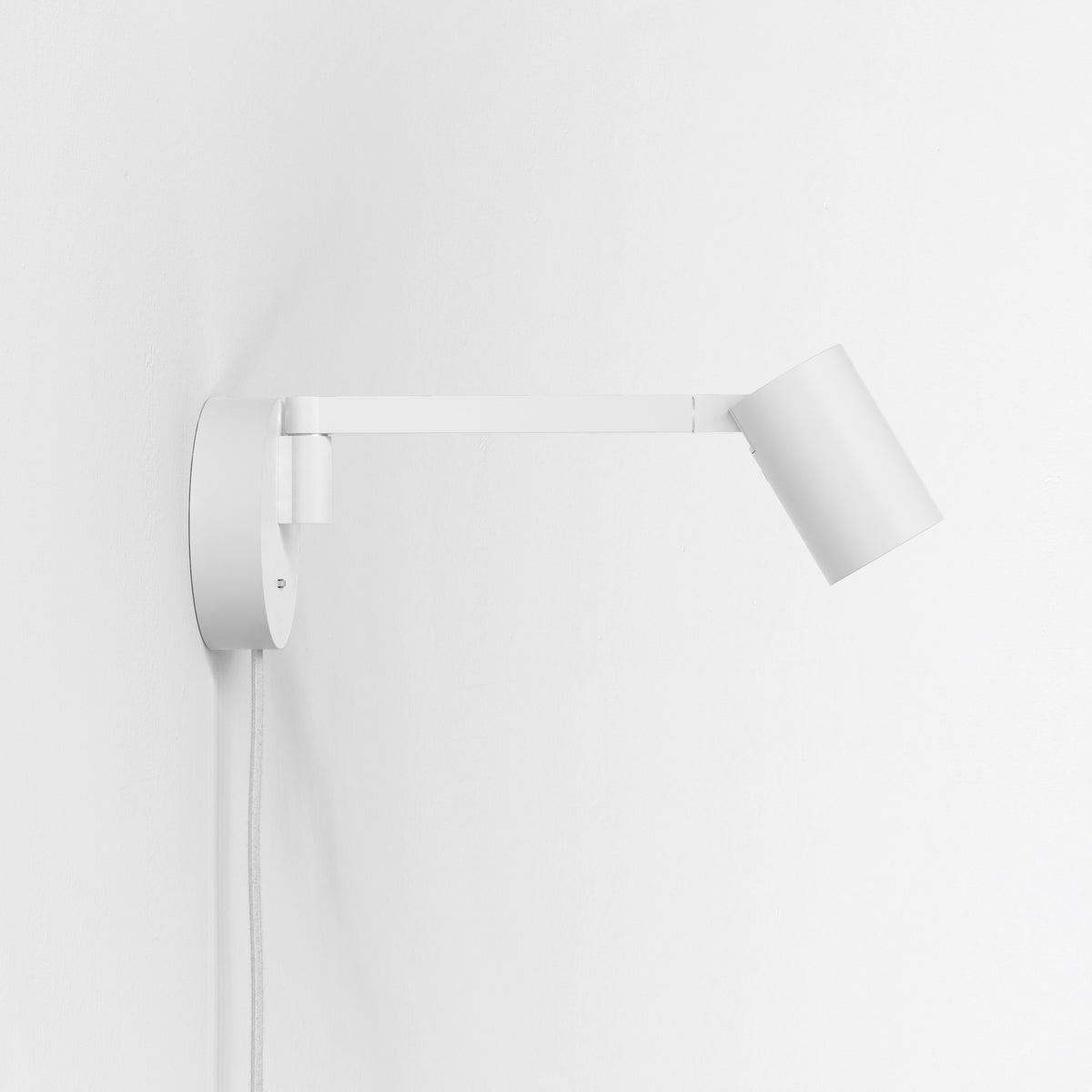 White wall-mounted lamp with an adjustable arm and cylindrical head, against a plain white wall