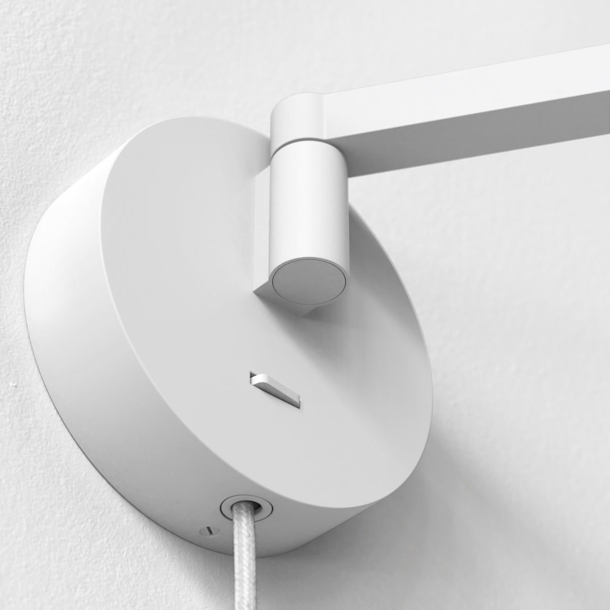 White wall lamp with a round base and an articulated arm, a braided cable extends from the base