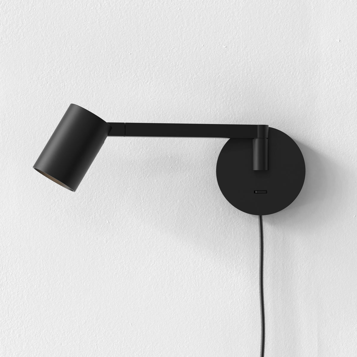 Black wall-mounted lamp with an adjustable arm and a cylindrical head, against a white textured wall