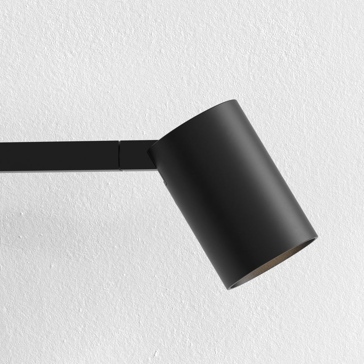 Black cylindrical spotlight on a black track against a white textured wall