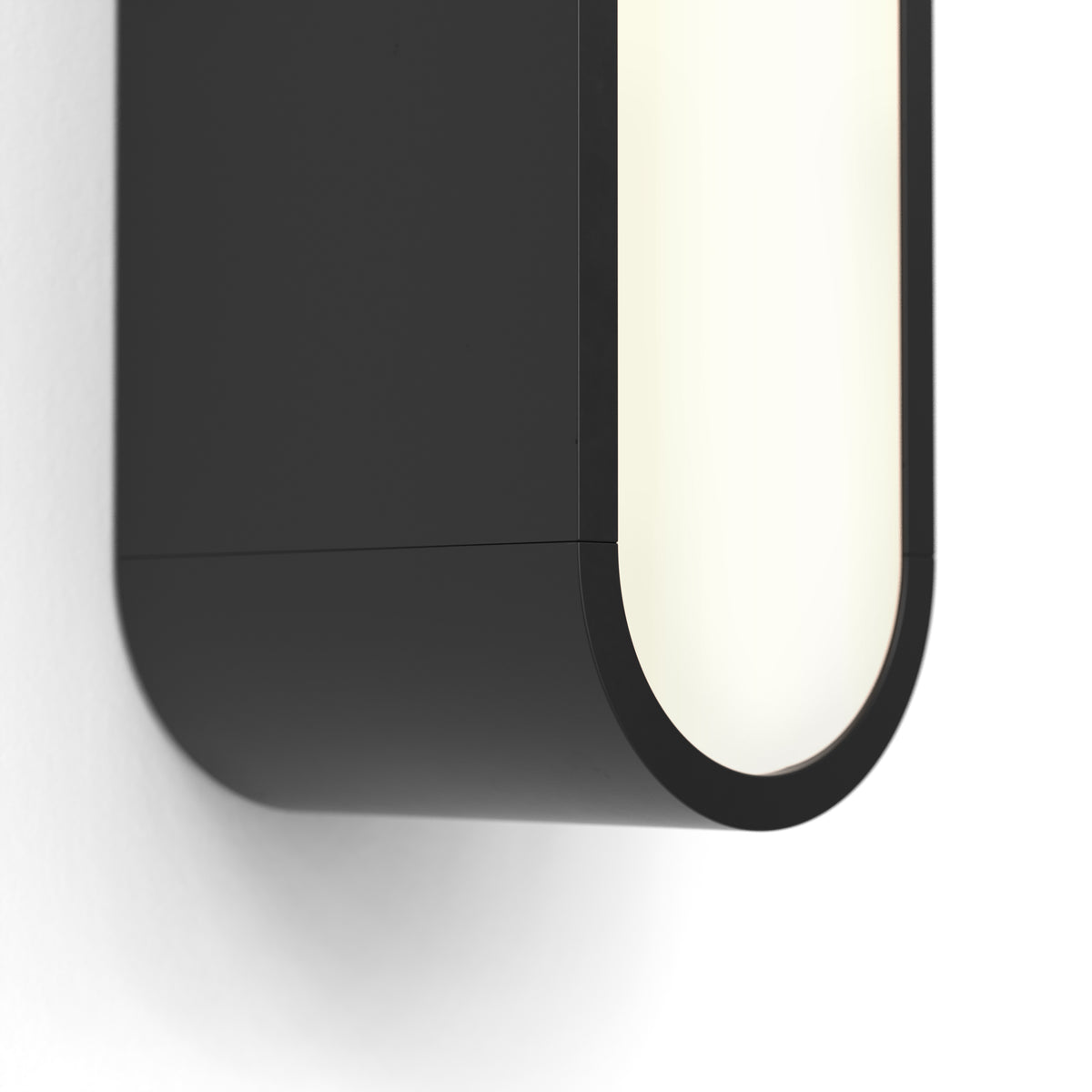 Close up of a black wall light with a rounded rectangular shape and a bright white light