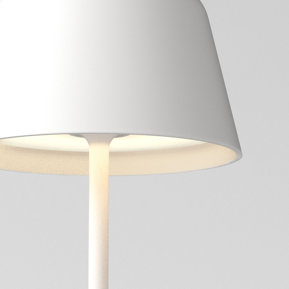 Close-up of a white table lamp with a conical shade, emitting a warm glow