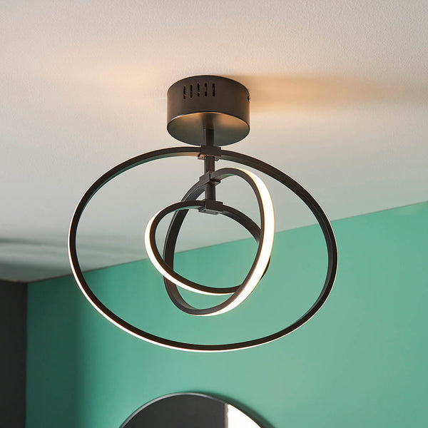 Modern black ceiling light with three intertwined oval rings, two of which are illuminated, against a teal wall.