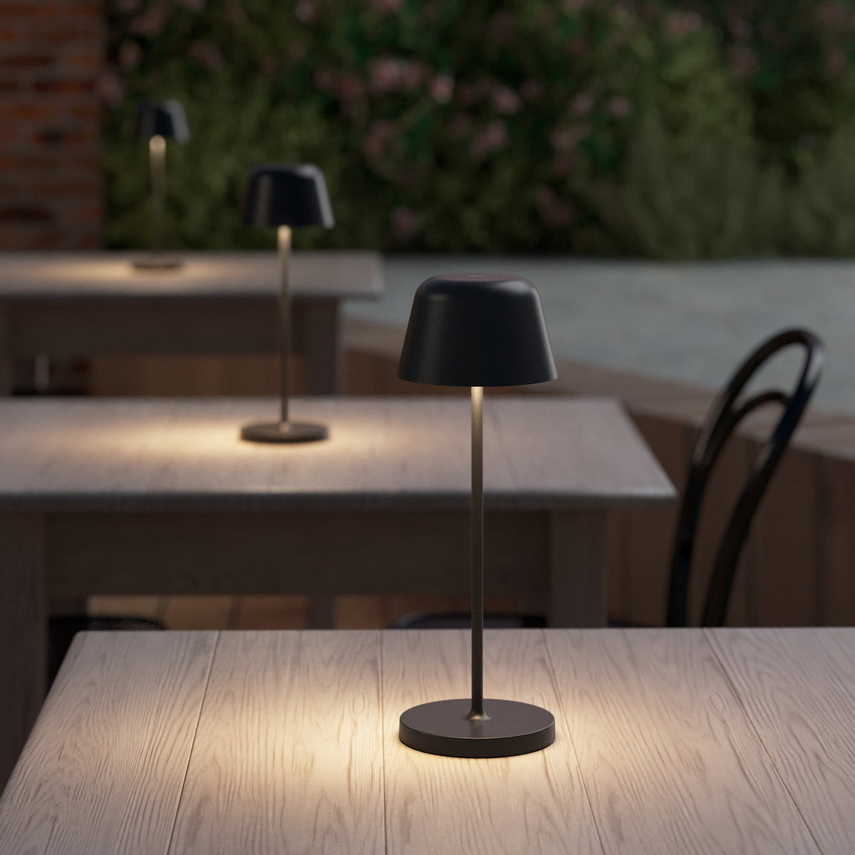 Black table lamps illuminate wooden tables in an outdoor restaurant setting at dusk