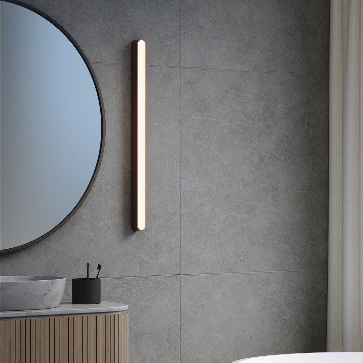 Bathroom with round mirror, vertical light fixture, marble sink, wooden vanity, and grey tiled wall