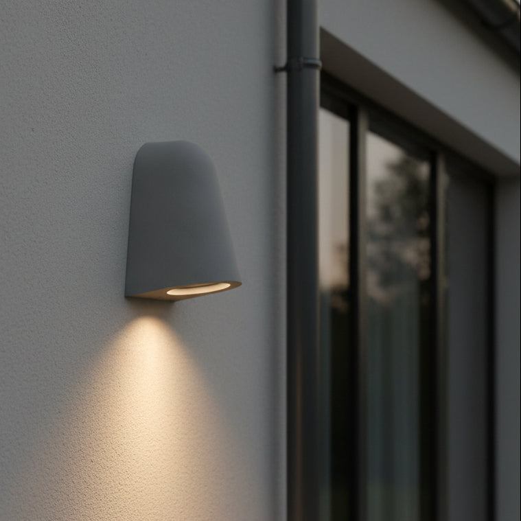 Grey outdoor wall light illuminating a textured wall next to a window and drainpipe
