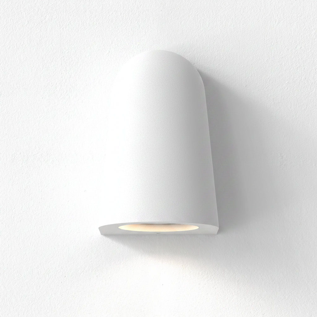 White wall light with a rounded top and a flat bottom, emitting a warm glow downwards onto a white wall