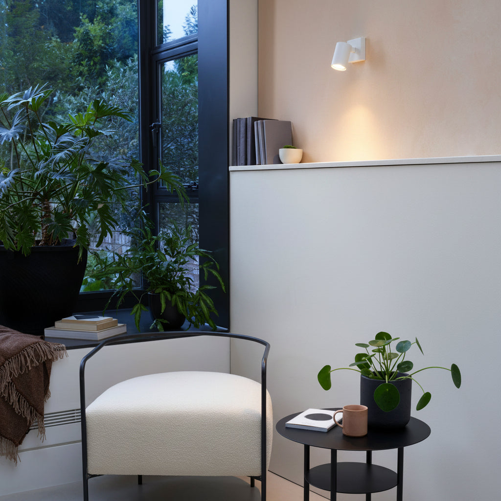 A cozy corner with a white armchair, a small black side table with a plant, and a large window overlooking trees