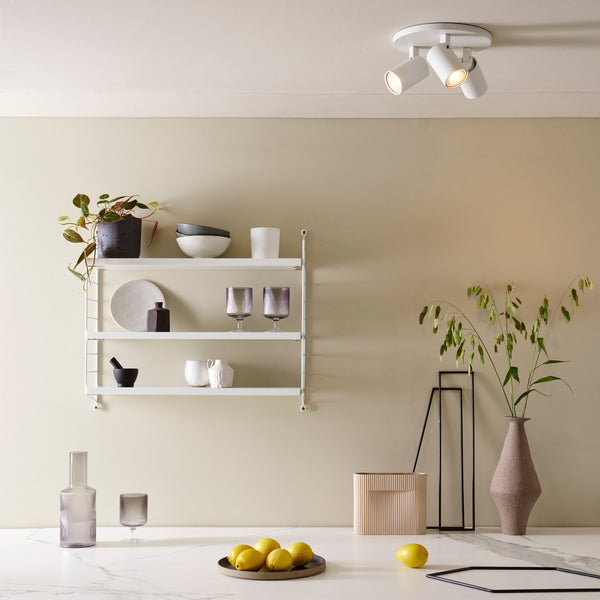 White ceiling light with three adjustable spotlights illuminating a room with a minimalist aesthetic